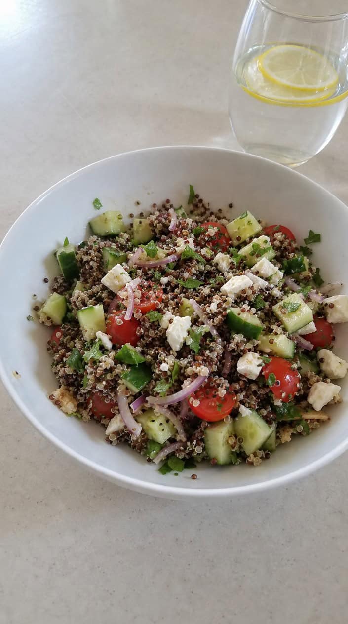 A bowl of colorful quinoa salad with feta cheese and fresh mint on a wooden table.