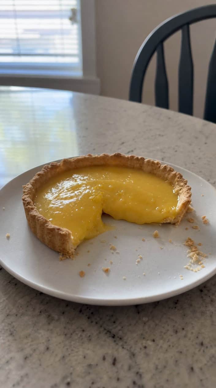 A lemon curd smash tart on a wooden table with baby boy themed decorations in soft blue and white around it.