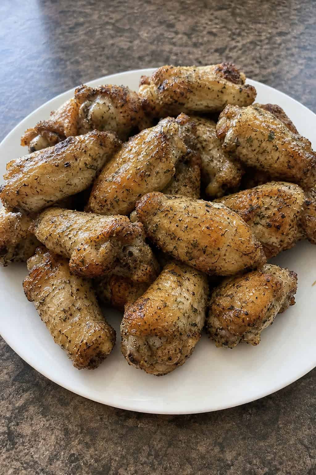 22 Chicken Wing Recipes for Game Day and Beyond 21 A plate of golden brown chicken wings coated with ranch seasoning and garnished with fresh dill on a wooden table.