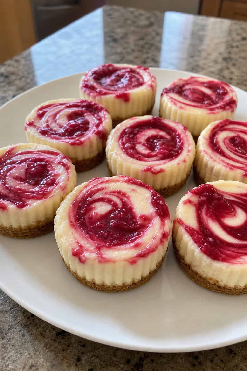 Plate of raspberry swirl mini cheesecakes with fresh raspberries and mint leaves on a festive table.