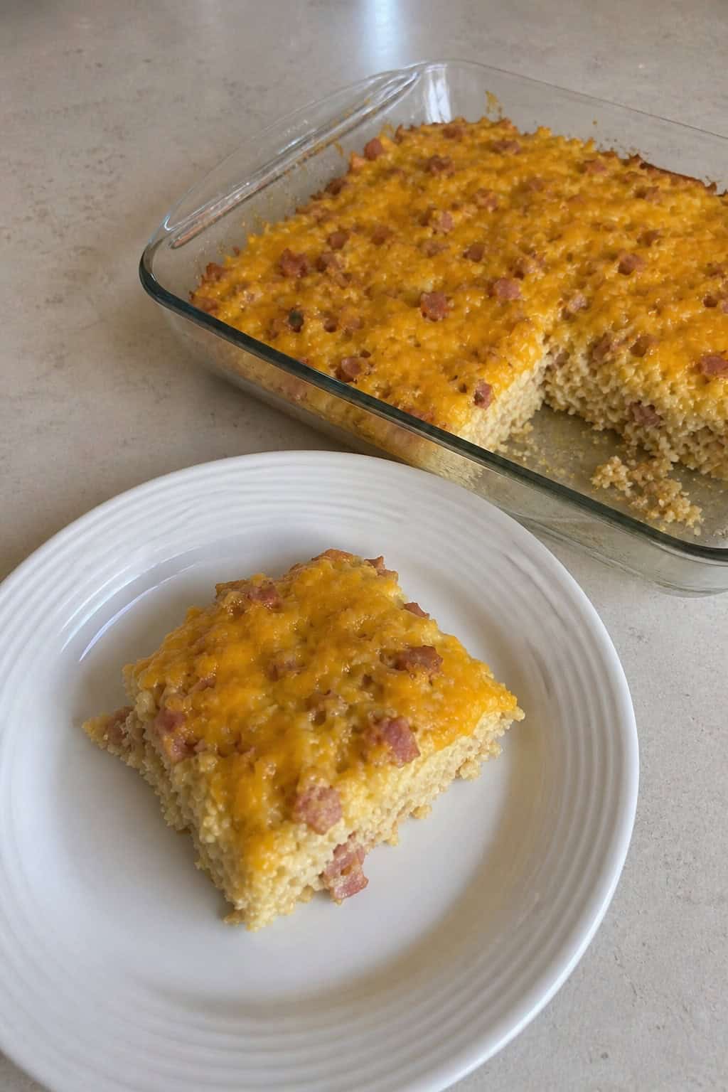 A breakfast casserole in a ceramic dish on a kitchen table, with a packed backpack visible near the door and a coffee mug in the foreground.