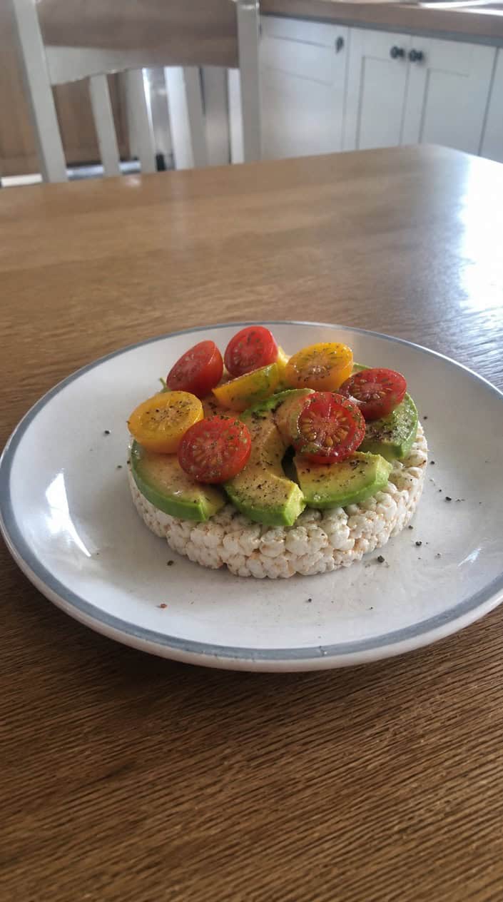 A rice cake topped with sliced avocado and cherry tomatoes on a white plate.