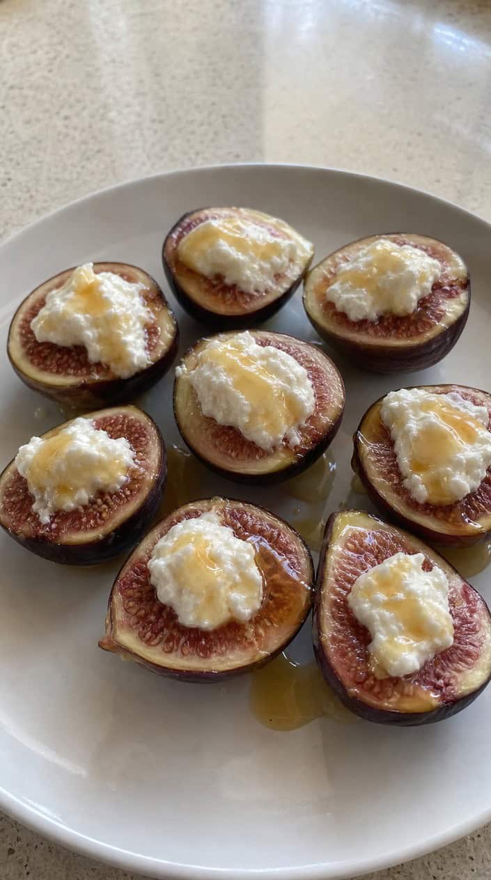 Close-up of halved figs stuffed with ricotta and drizzled with honey on a plate outdoors during golden hour.
