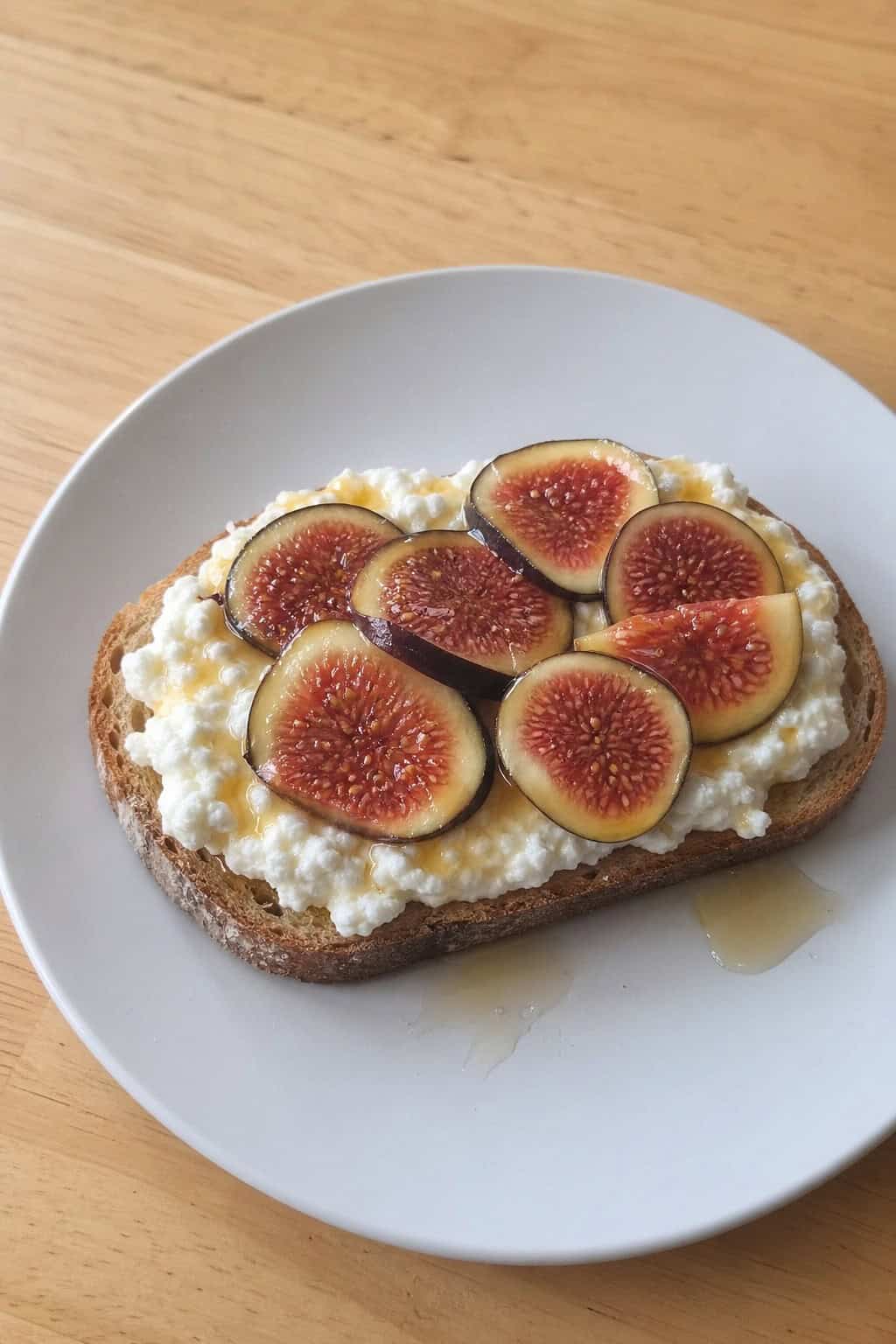 A slice of ricotta toast topped with fresh fig slices and honey on a plate.