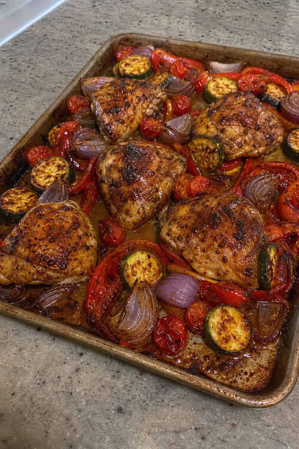 25 Chicken Thigh Recipes for Easy Weeknight Dinners 7 Sheet pan with BBQ ranch chicken thighs and roasted vegetables on a wooden table.