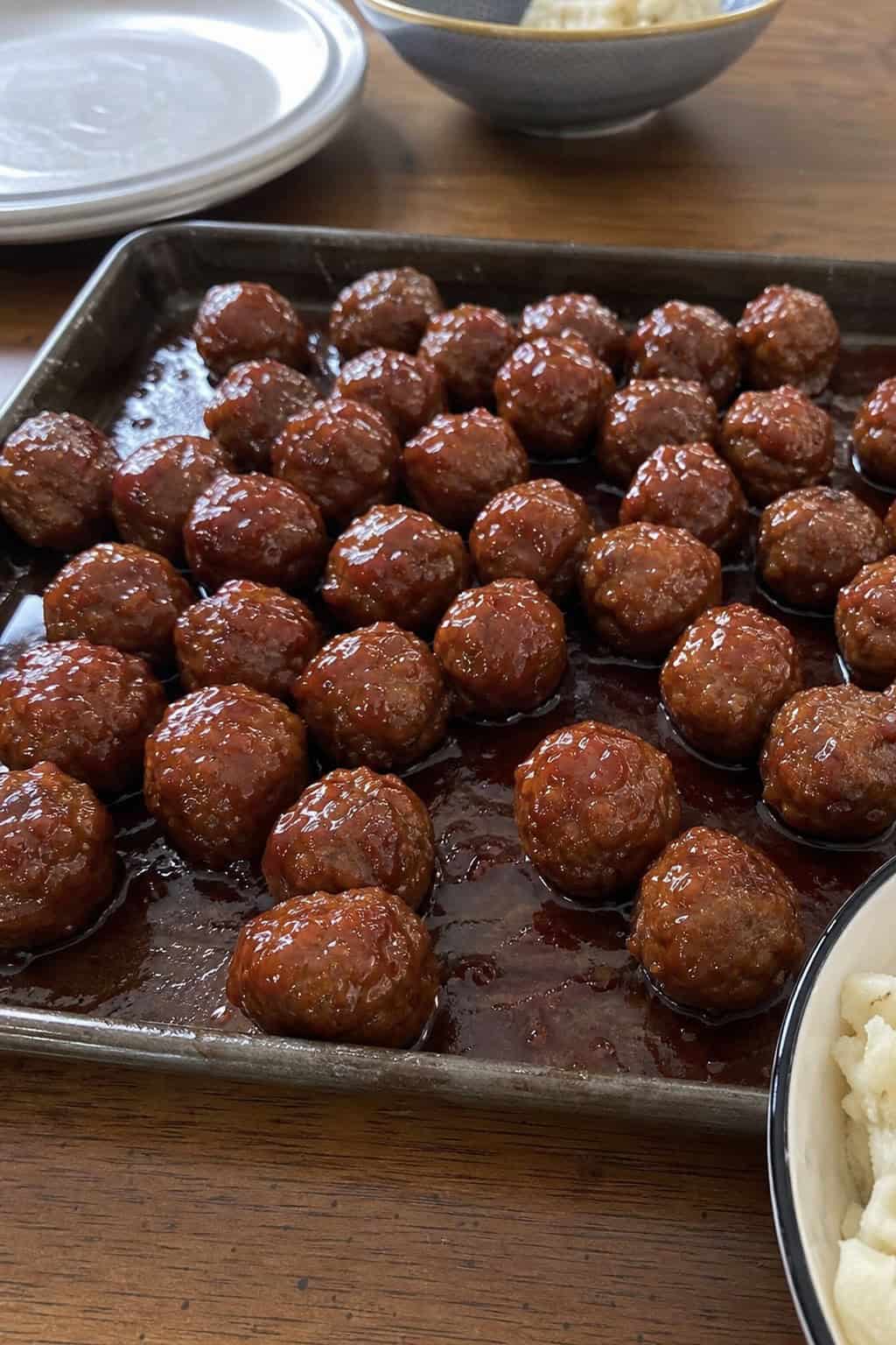 Sheet pan filled with glazed meatballs coated in grape jelly and chili sauce, ready to be served as a party appetizer.