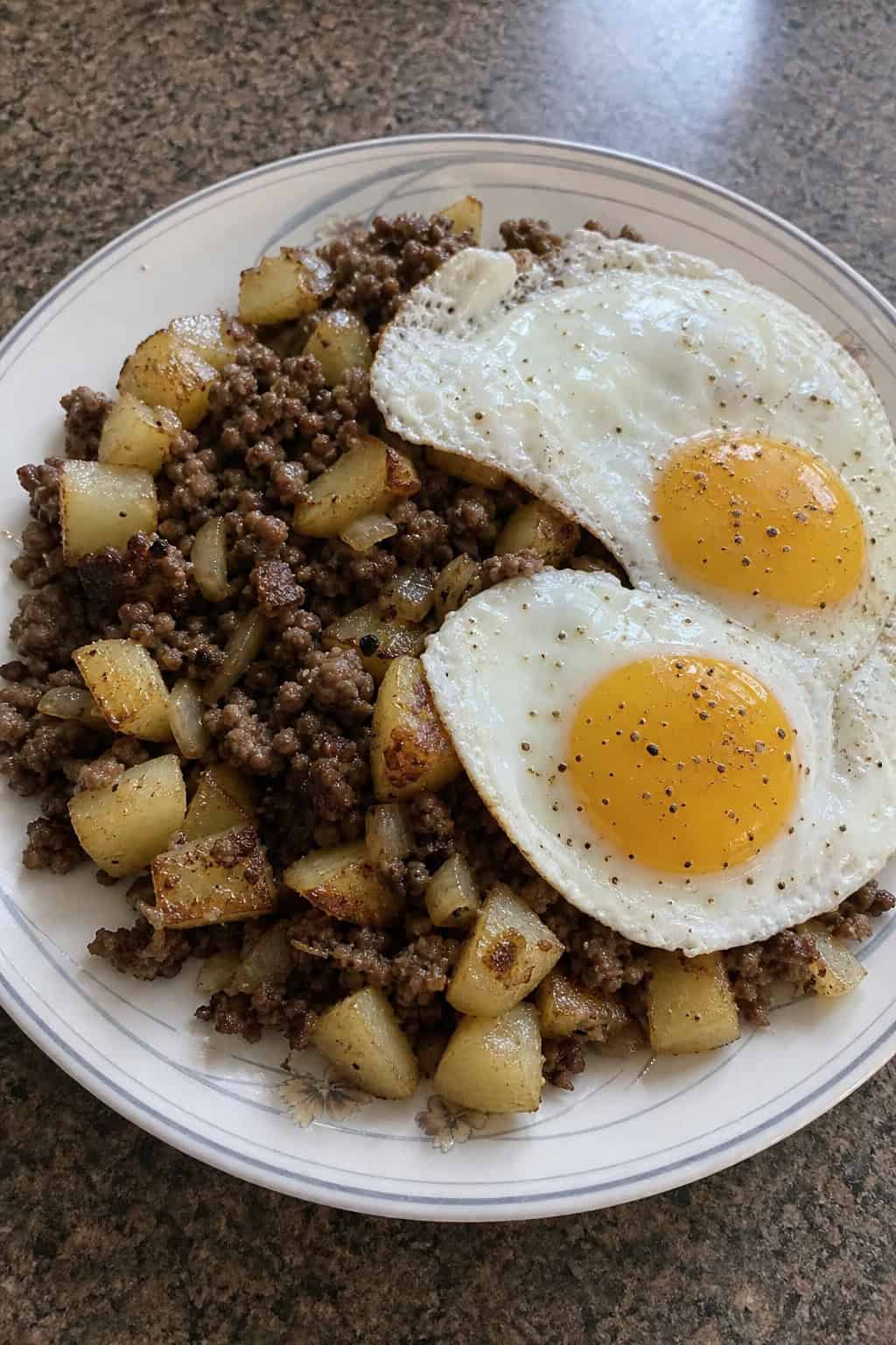 A plate of beef and potato hash topped with two fried eggs on a wooden table.