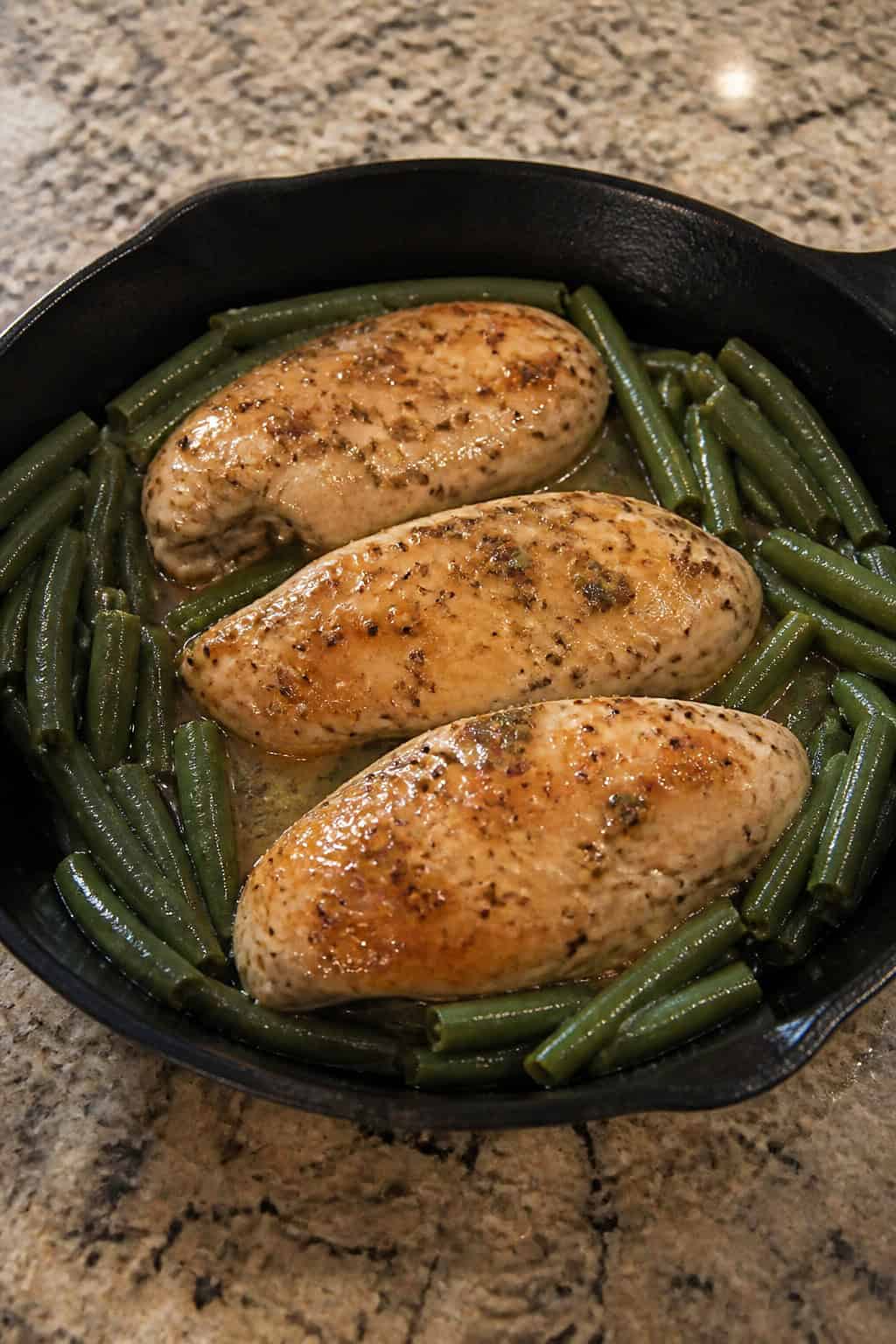 A skillet with honey-mustard glazed chicken breasts and green beans on a wooden table.