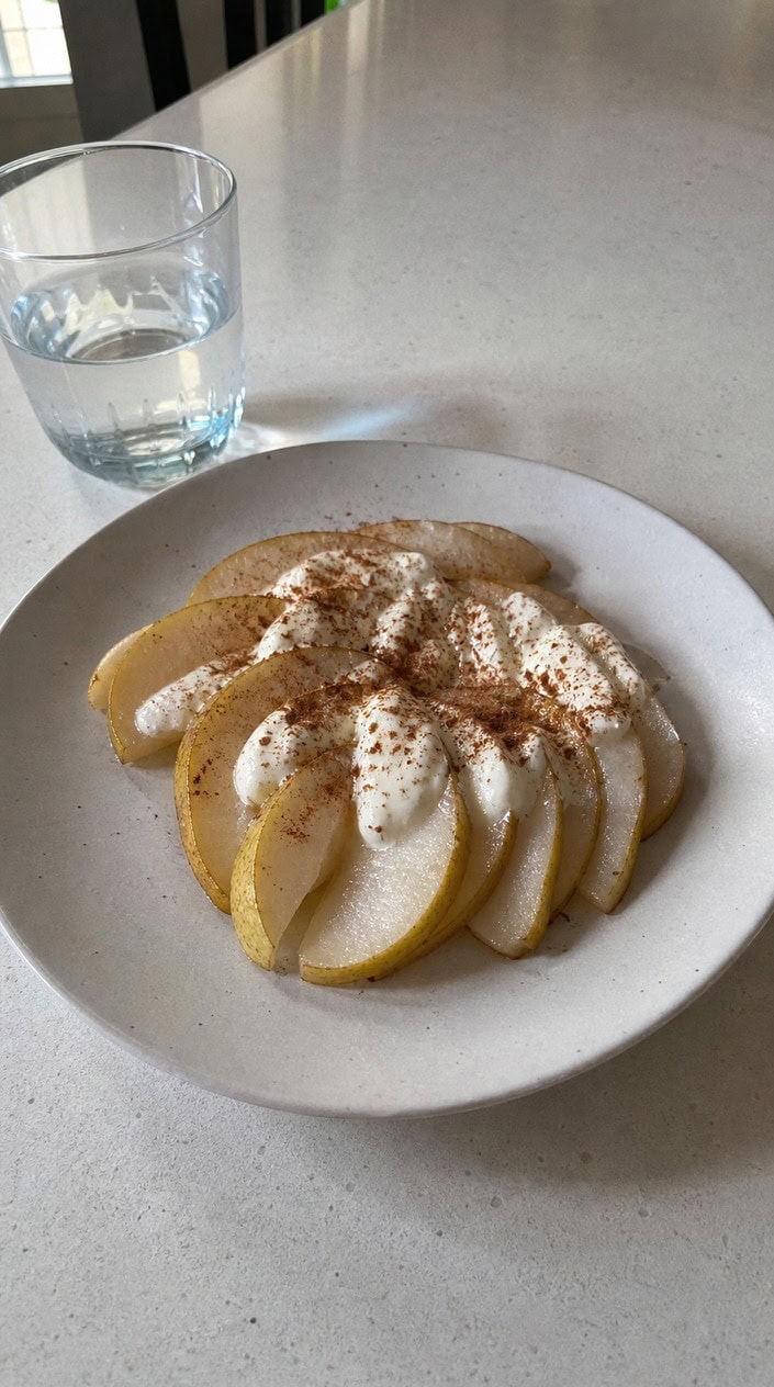 A plate with sliced pear topped with ricotta cheese and sprinkled cinnamon on a wooden table.