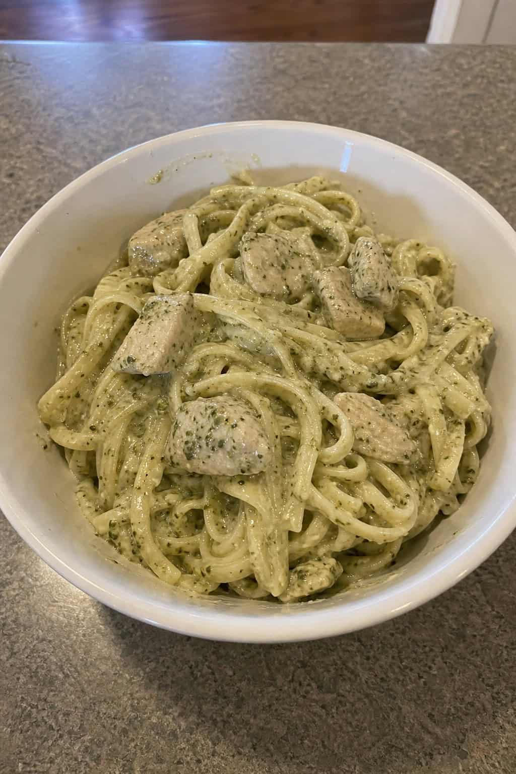 A bowl of creamy pesto chicken pasta garnished with fresh basil on a wooden table with fresh ingredients around it.