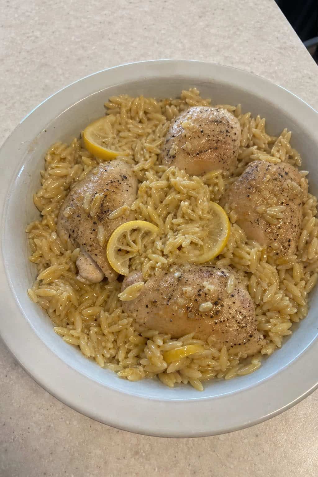 Slow cooker filled with lemon garlic chicken and orzo pasta garnished with fresh herbs on a wooden table.