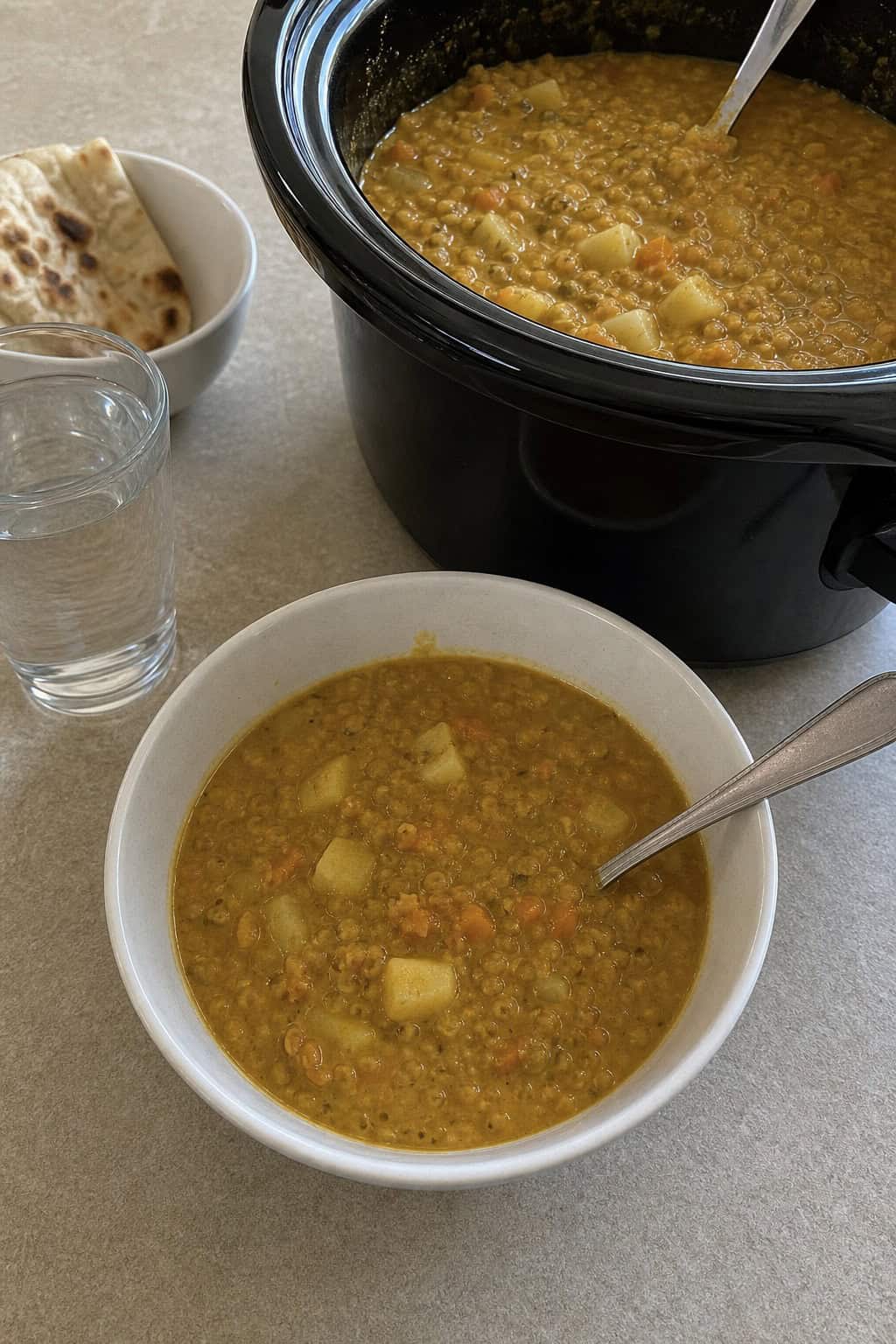 Slow cooker filled with curried lentil and apple soup on a kitchen countertop surrounded by fresh ingredients.
