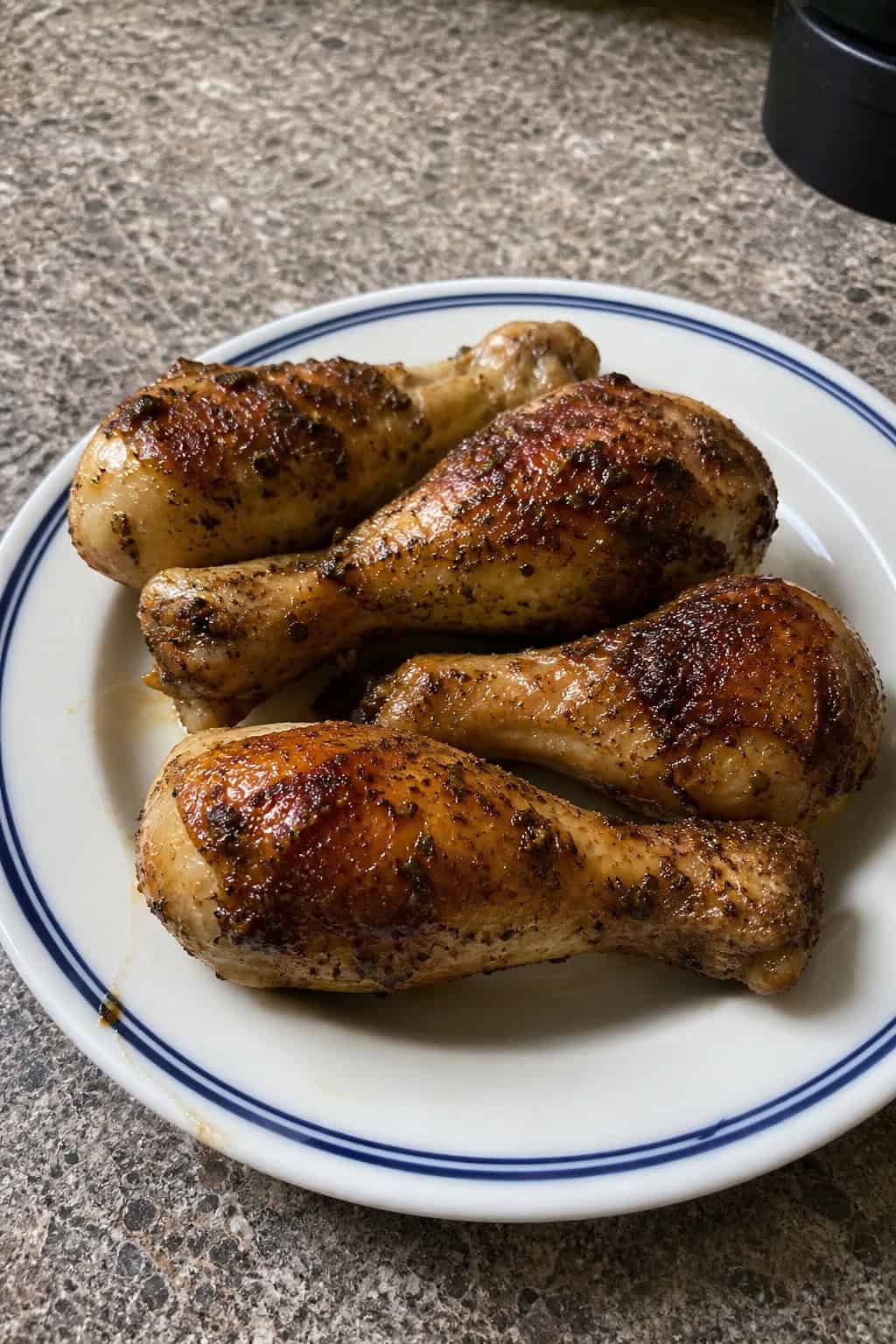 Easy Chicken Leg Recipes for Family Dinners 21 Golden-brown slow-roasted chicken legs on a wooden platter with crispy herb-speckled skin, fresh rosemary and thyme, and lemon wedges arranged alongside.