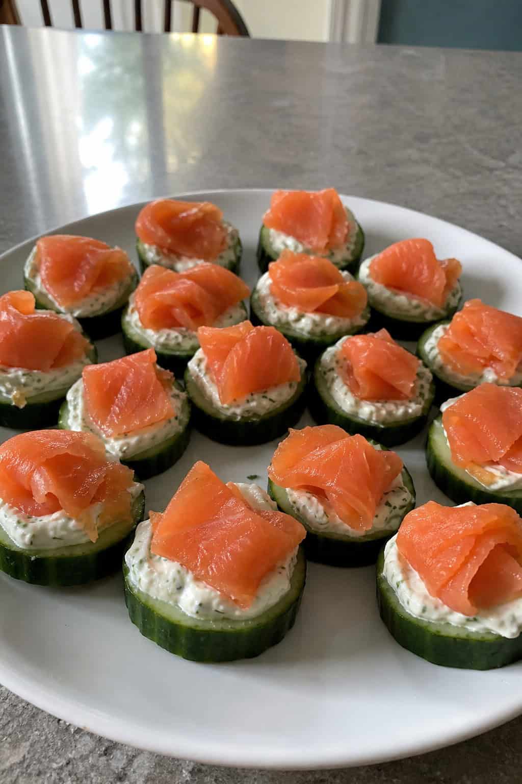 A platter of cucumber slices topped with dill cream cheese and smoked salmon, garnished with fresh dill, on a wooden table.