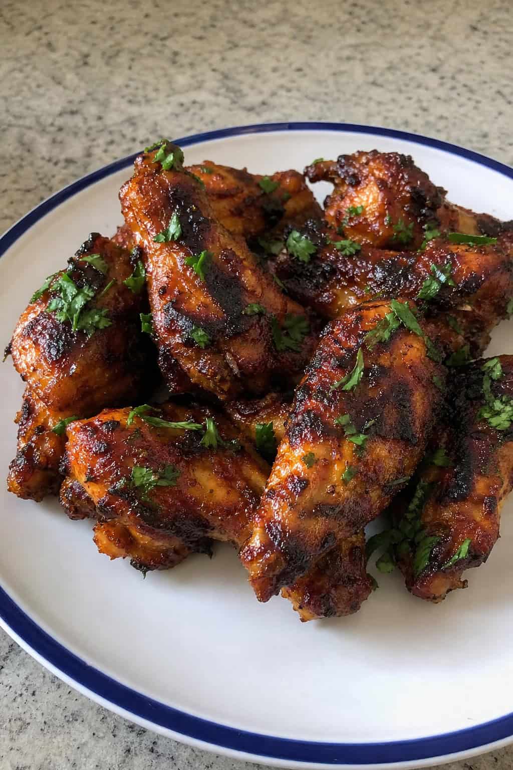 Plate of smoky chipotle lime chicken wings garnished with cilantro and lime wedges on a wooden table.