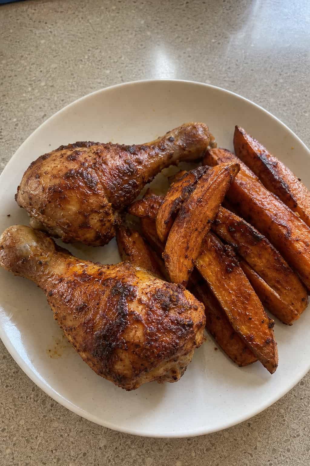 Roasted chicken legs with a deep red paprika crust alongside caramelized sweet potato wedges on a wooden serving board.