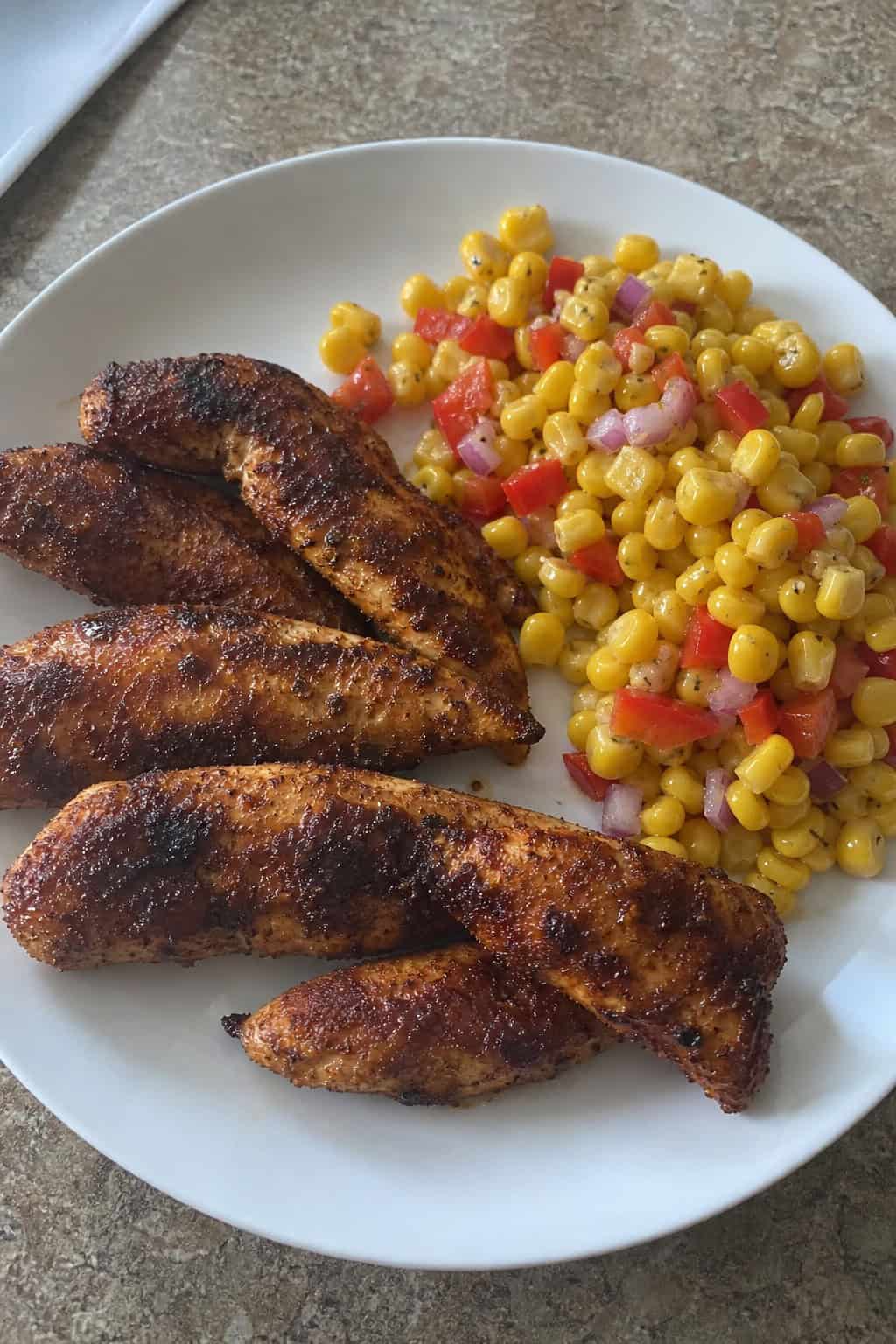 A plate of smoky paprika chicken tenders served with a fresh corn salad on a wooden table.