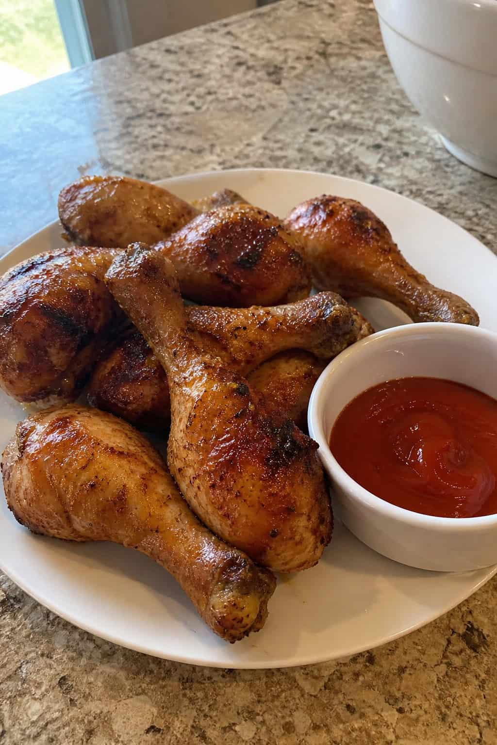 Deep brick-red smoky paprika roasted chicken drumsticks on a wood serving board, garnished with fresh flat-leaf parsley, with small white bowls of dipping sauce on the side.