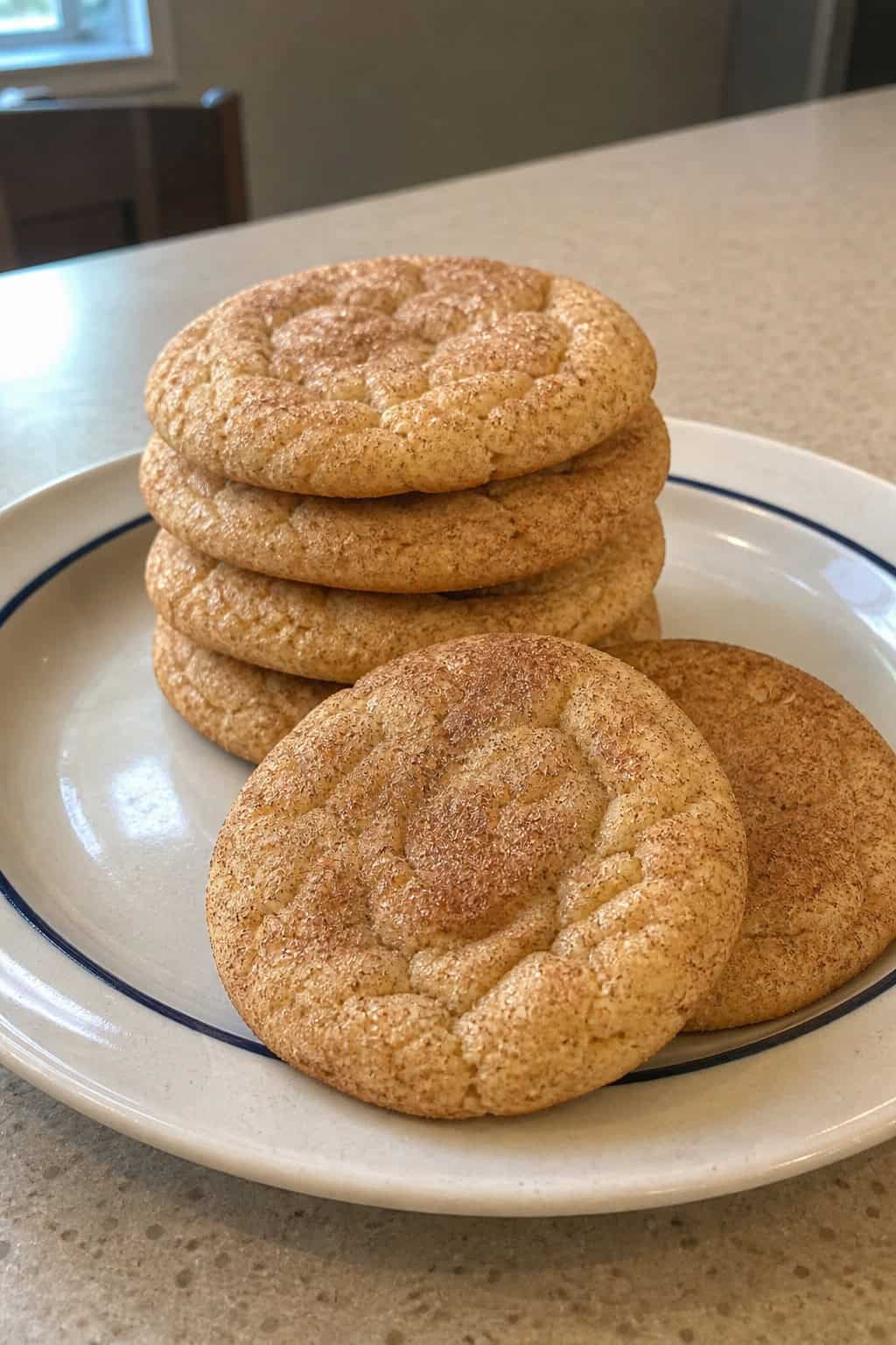 Close-up of freshly baked snickerdoodle cookies coated in cinnamon sugar on a wooden surface with cinnamon and sugar bowls nearby.