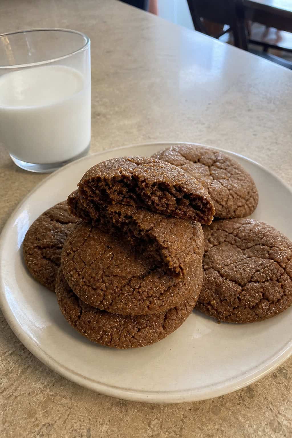 A stack of soft molasses cookies on a wooden surface with cinnamon sticks and molasses nearby.