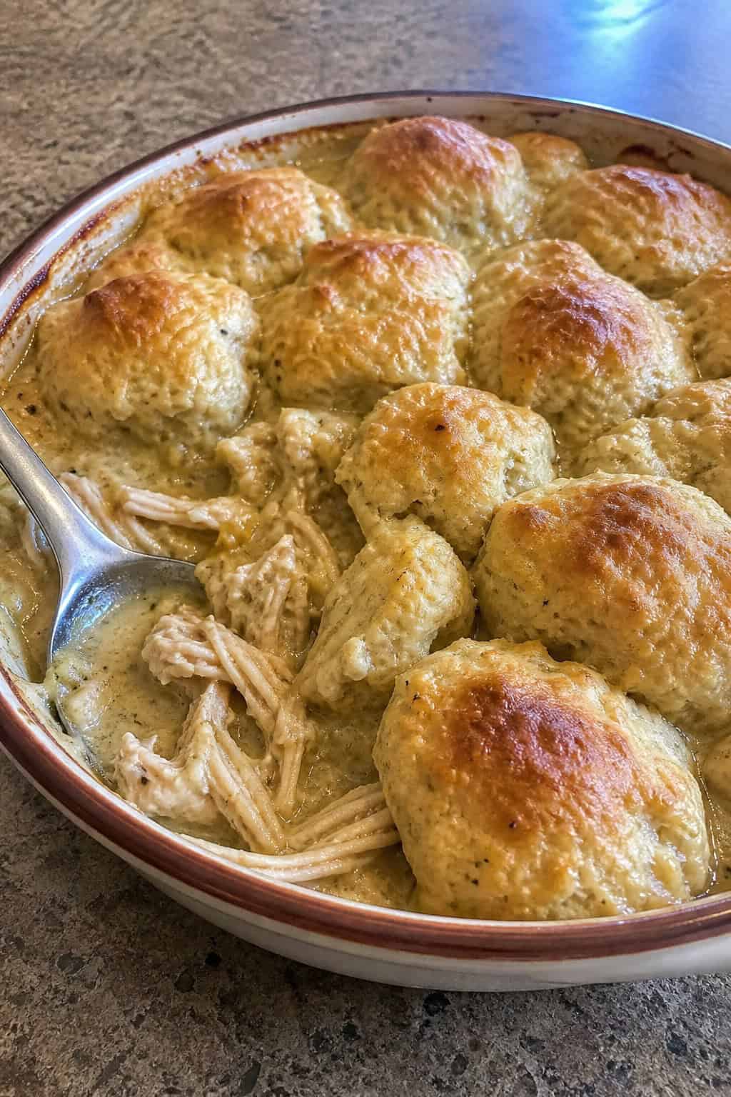 A golden-brown Southern chicken and dumpling casserole in a deep ceramic dish on a wooden table, with fluffy Bisquick dumplings puffed across the top and fresh thyme nearby.