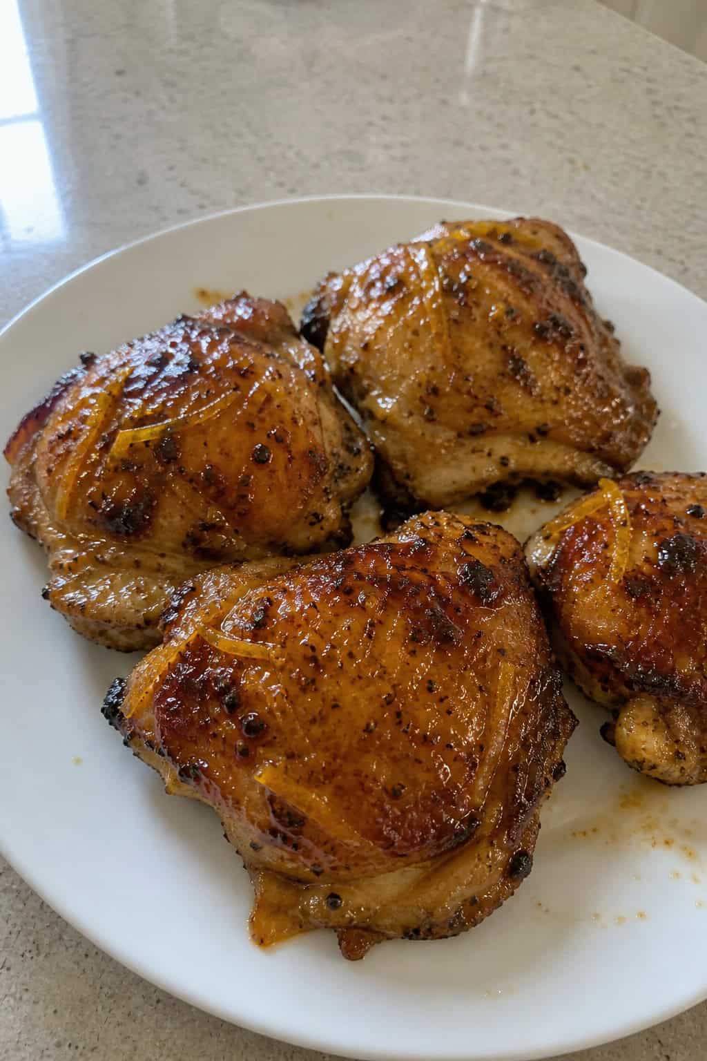 A plate of glazed chicken thighs garnished with rosemary and orange slices on a wooden table.