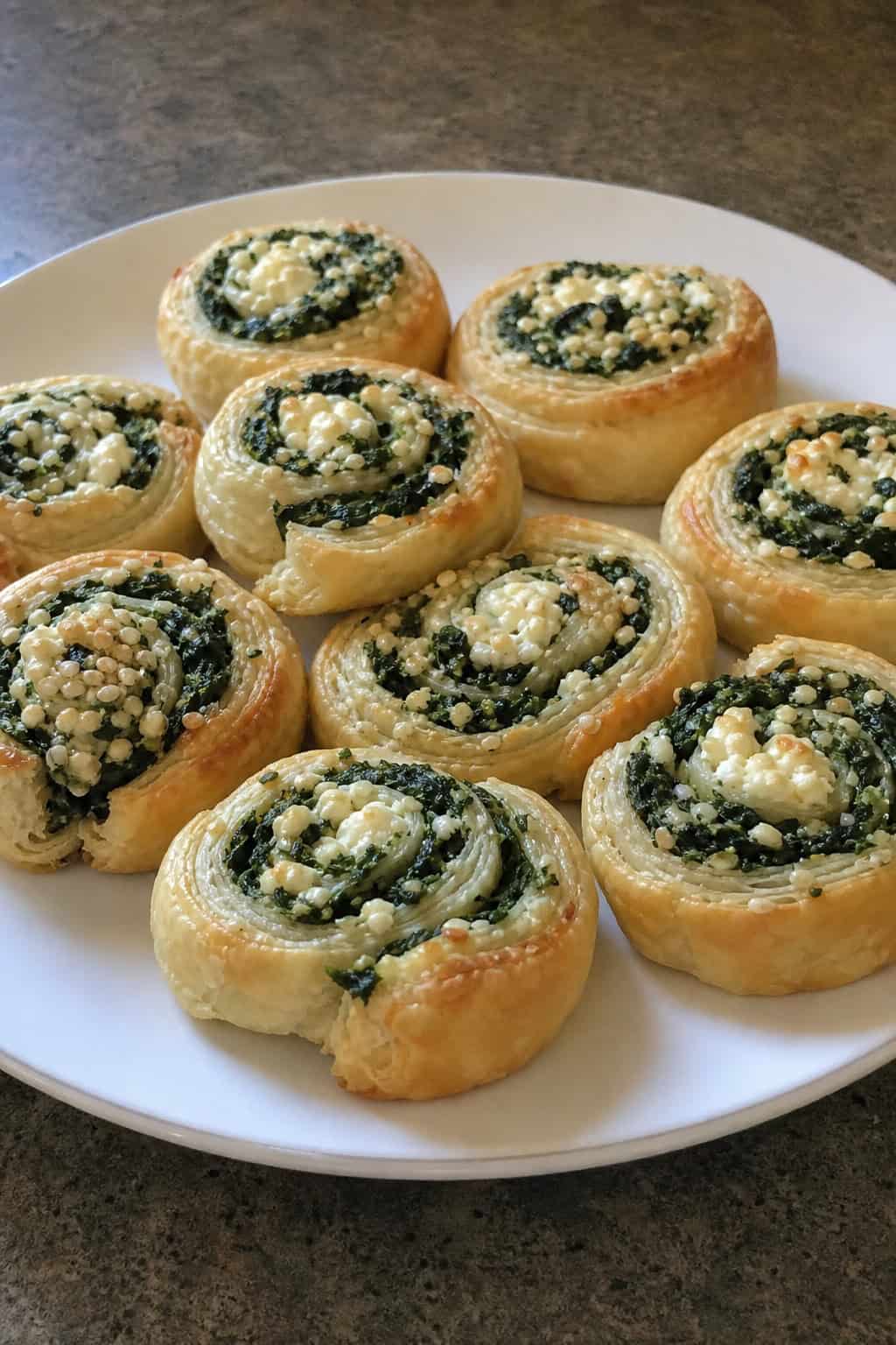 Close-up of golden puff pastry pinwheels filled with spinach and feta cheese arranged on a wooden board.