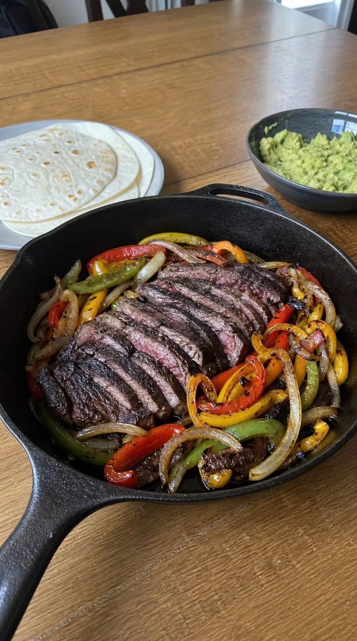 A plate of grilled steak fajitas with charred peppers and onions on a wooden table outdoors.