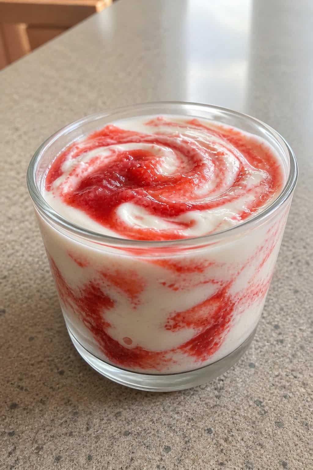 A glass cup filled with creamy cheesecake pudding swirled with strawberry sauce, topped with fresh strawberries and mint on a wooden surface.