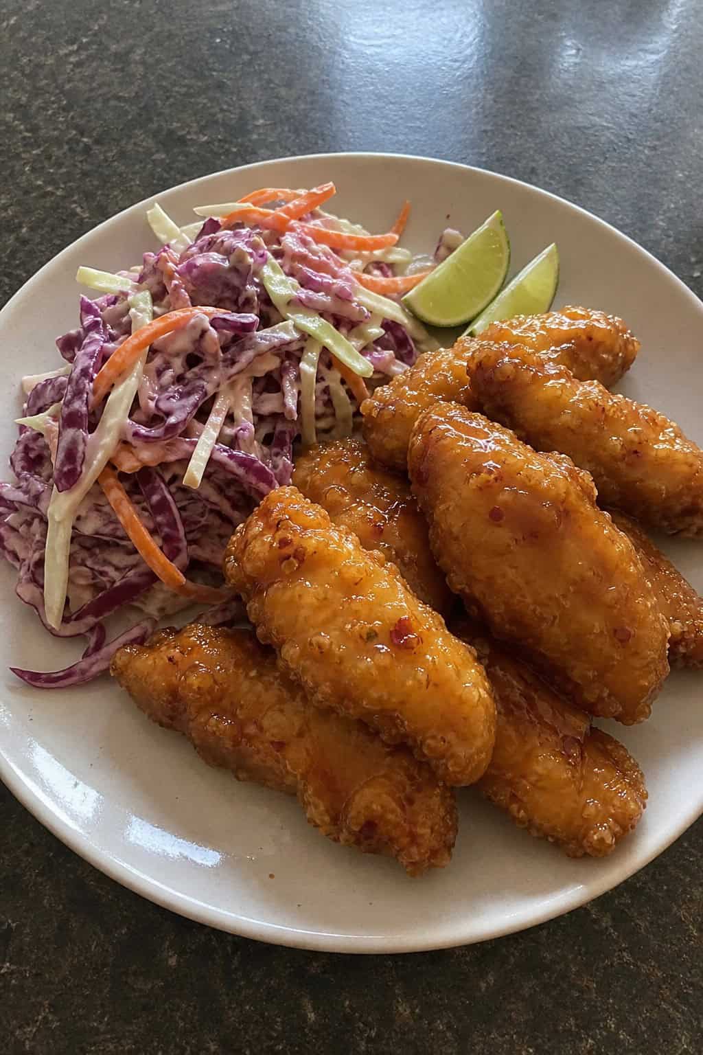 A plate of crispy sweet chili lime chicken tenders served with fresh colorful slaw on a wooden table.