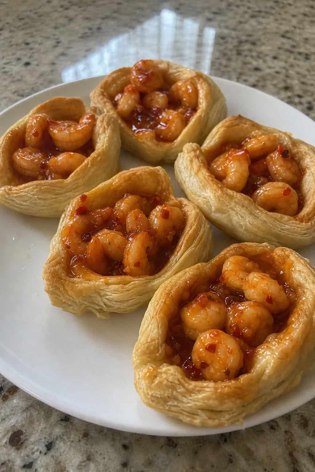 Close-up of several puff pastry boats filled with sweet chili shrimp, garnished with fresh herbs, arranged on a wooden board.