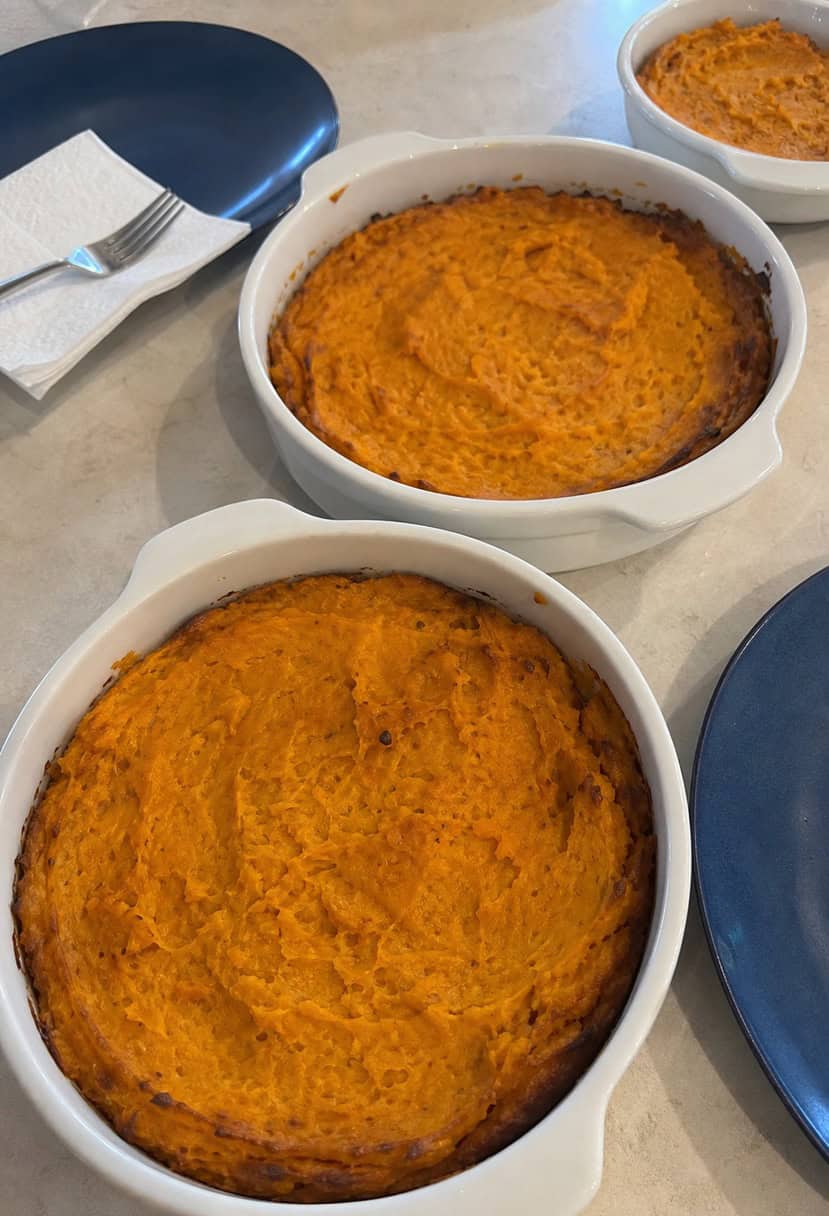 A table spread with various sweet potato casserole dishes, surrounded by ingredients and kitchen utensils