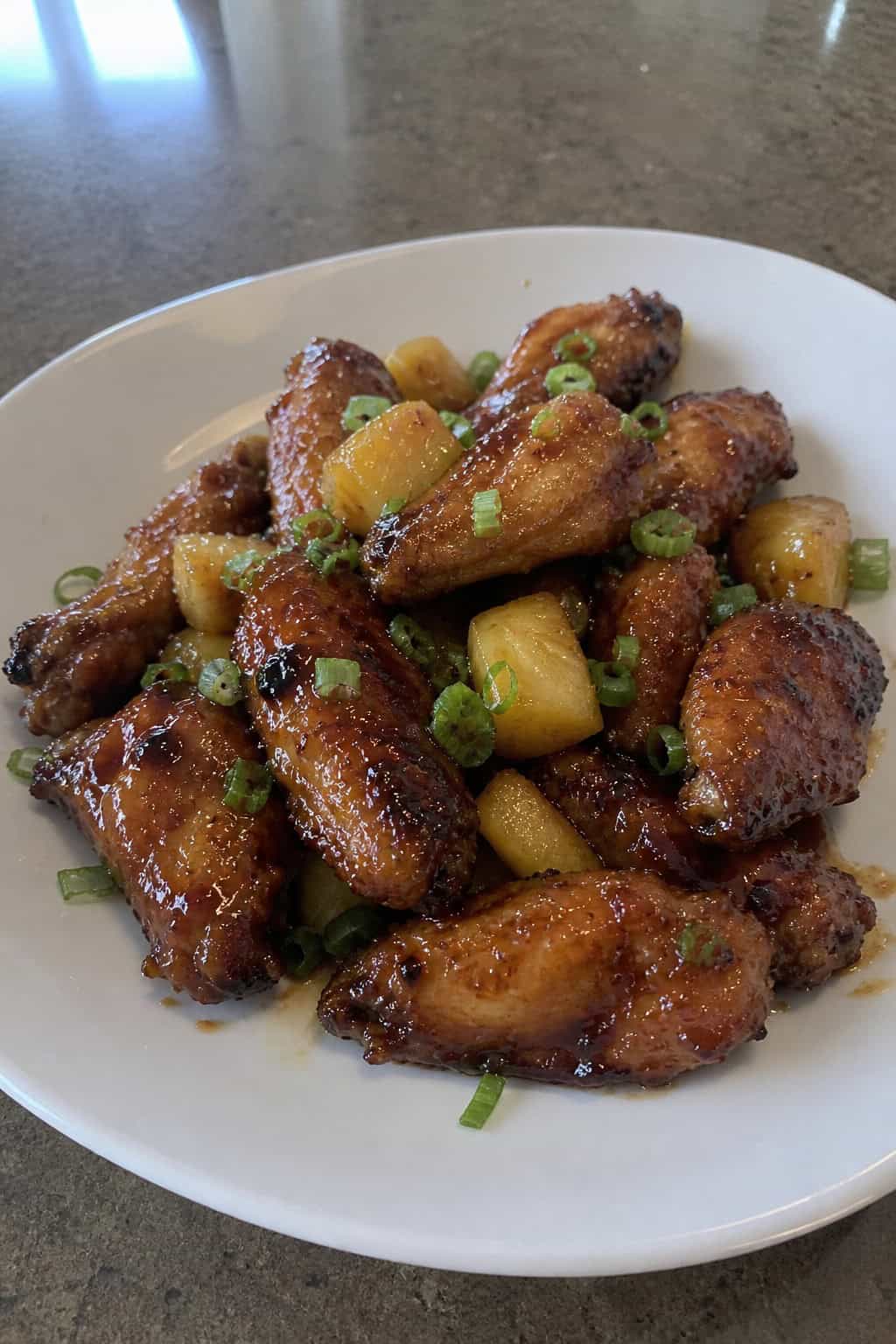 A plate of crispy teriyaki chicken wings garnished with pineapple chunks and green onions.