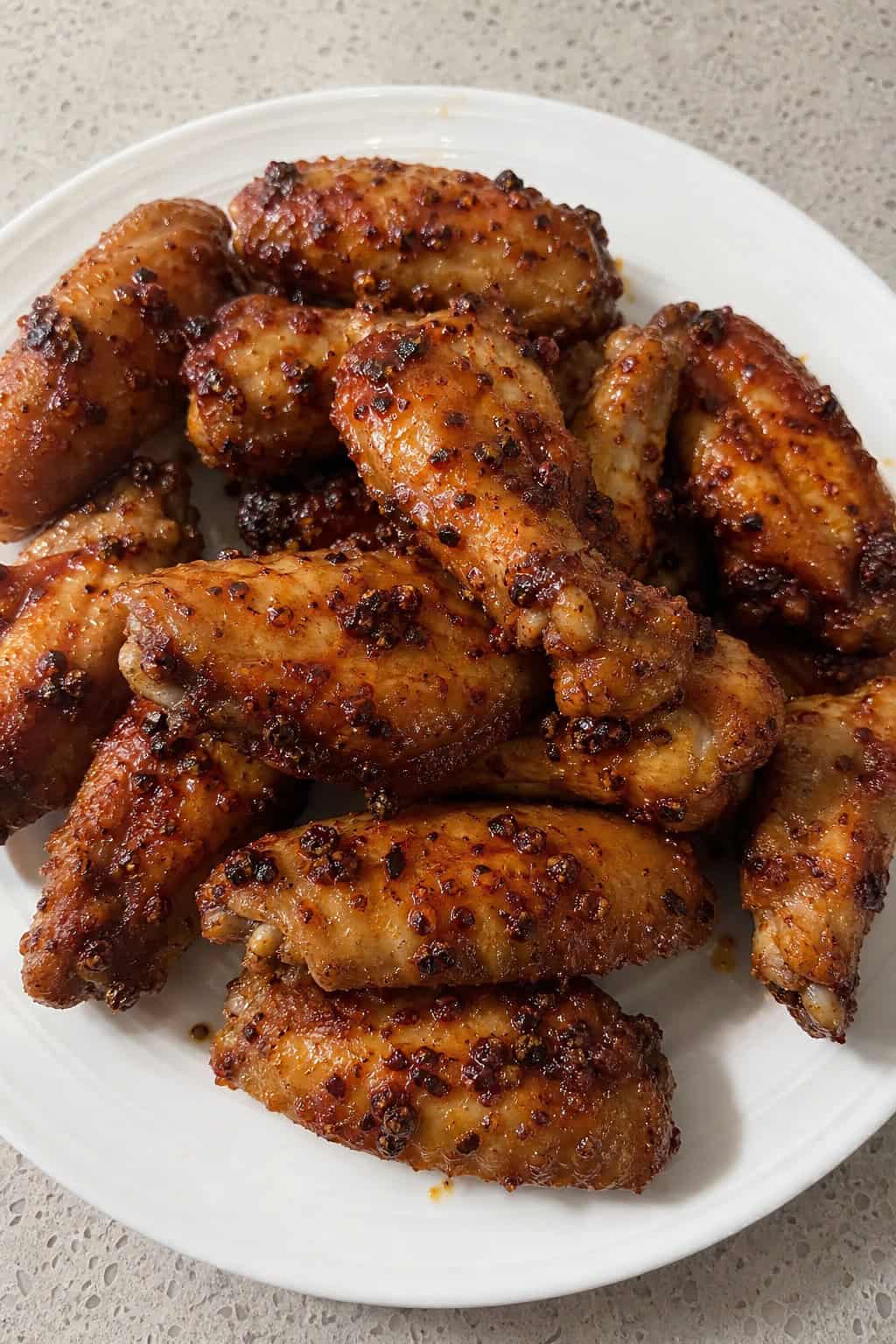 A plate of spicy Szechuan peppercorn chicken wings garnished with scallions and accompanied by a small bowl of dipping sauce.