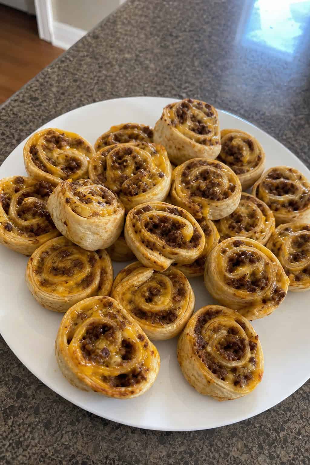 A platter of taco-seasoned beef and cheddar pinwheel appetizers showing seasoned ground beef and melted orange cheddar filling inside sliced flour tortilla rolls, with small dipping sauce bowls on a wooden board.