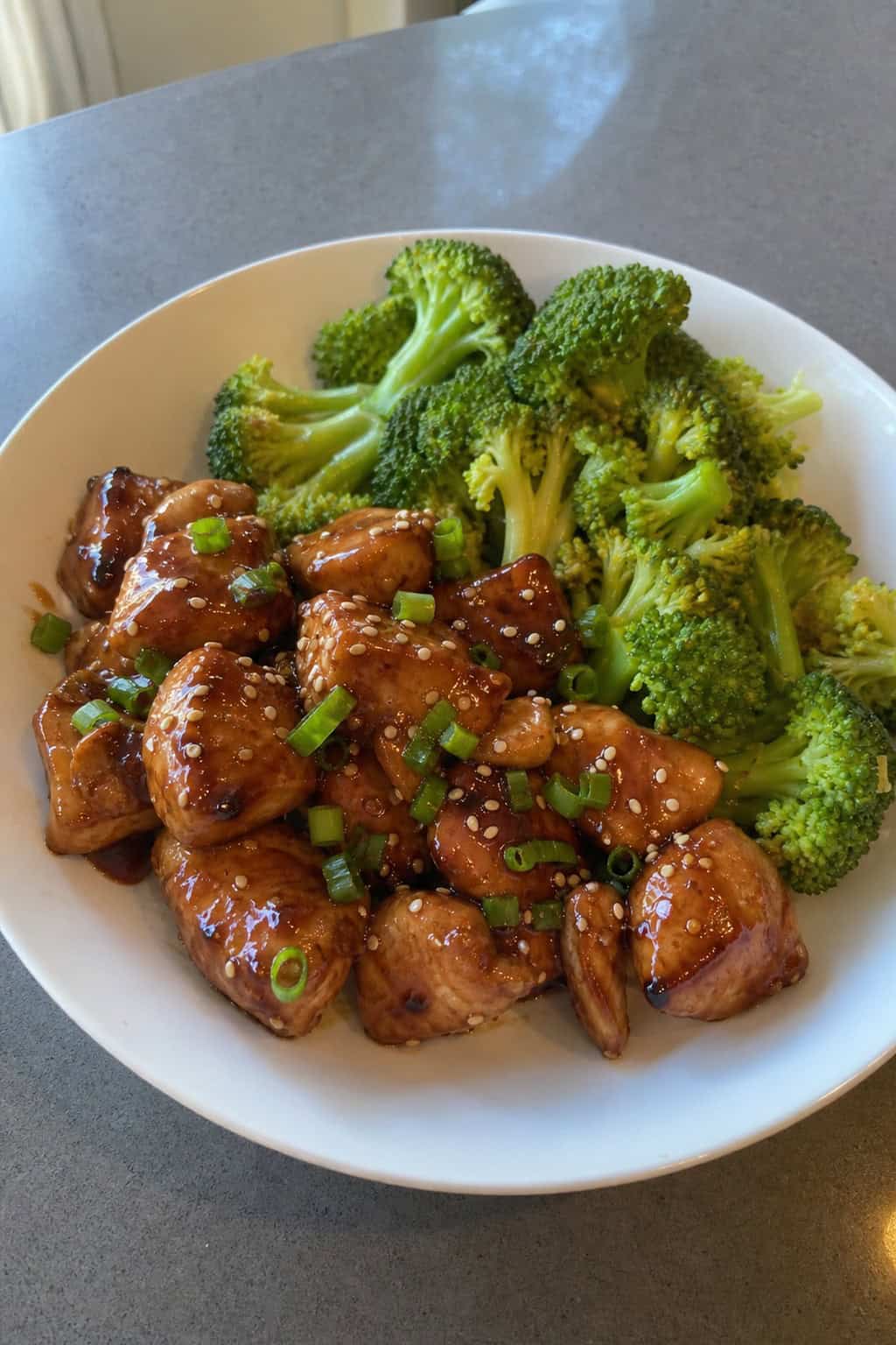 A bowl of teriyaki chicken with broccoli on a wooden table.