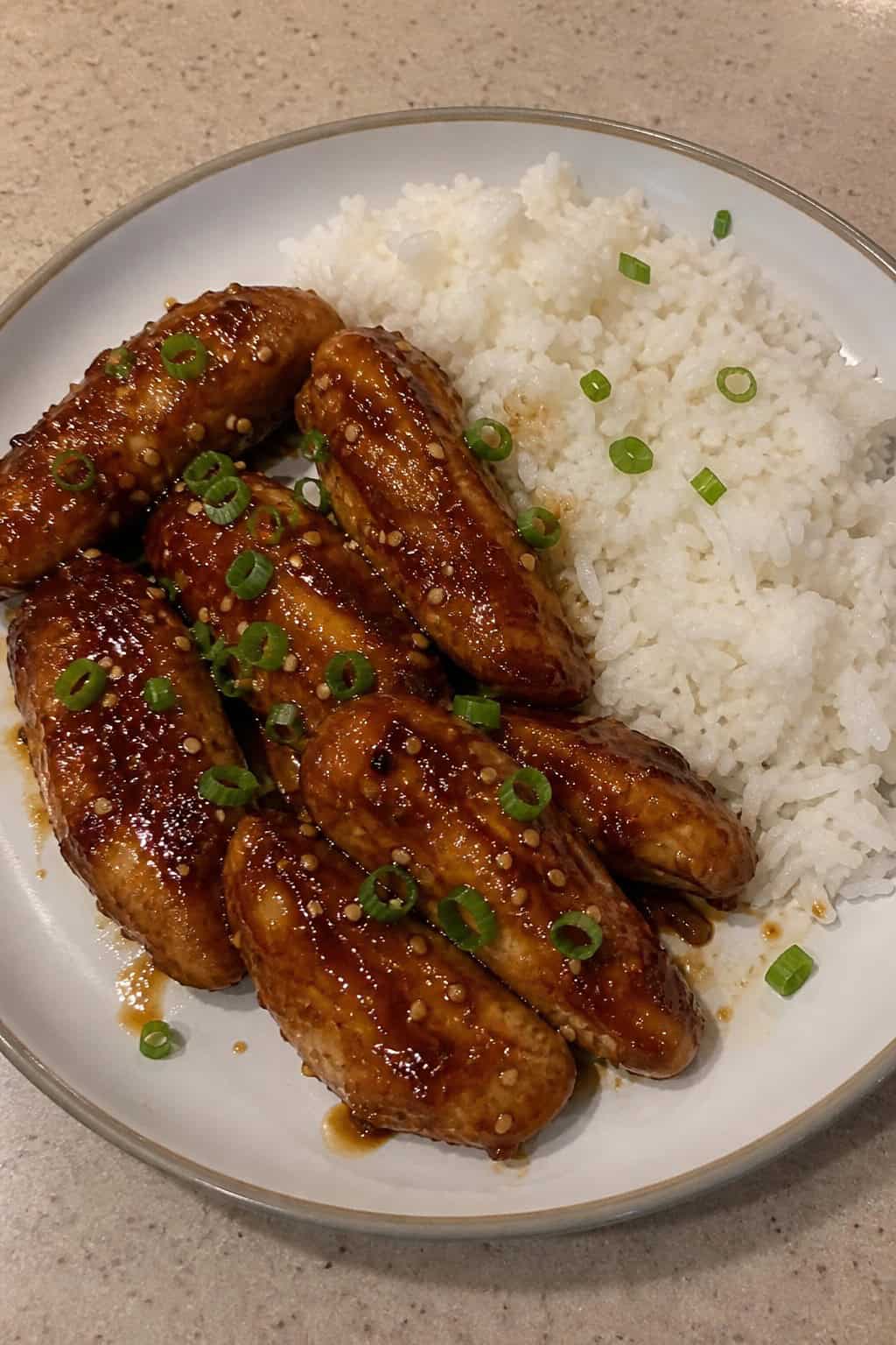 A plate of teriyaki sesame chicken tenders served with white rice on a wooden table.