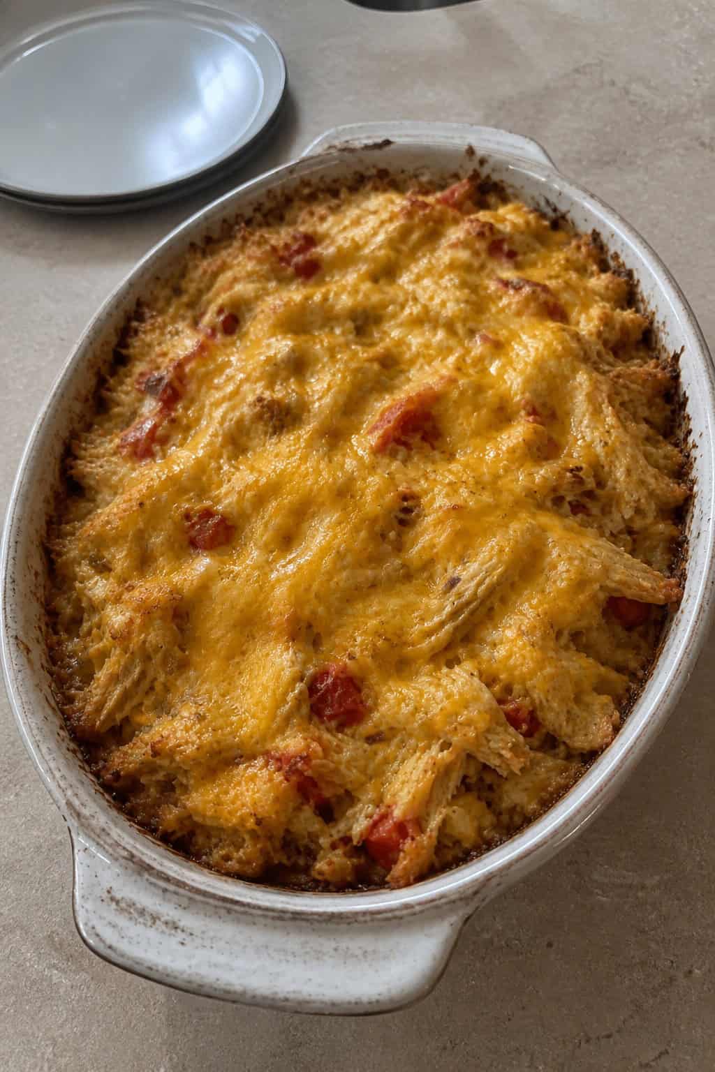 A freshly baked Tex-Mex chicken and hashbrown casserole in a ceramic dish on a wooden table with fresh herbs and lime wedges nearby.