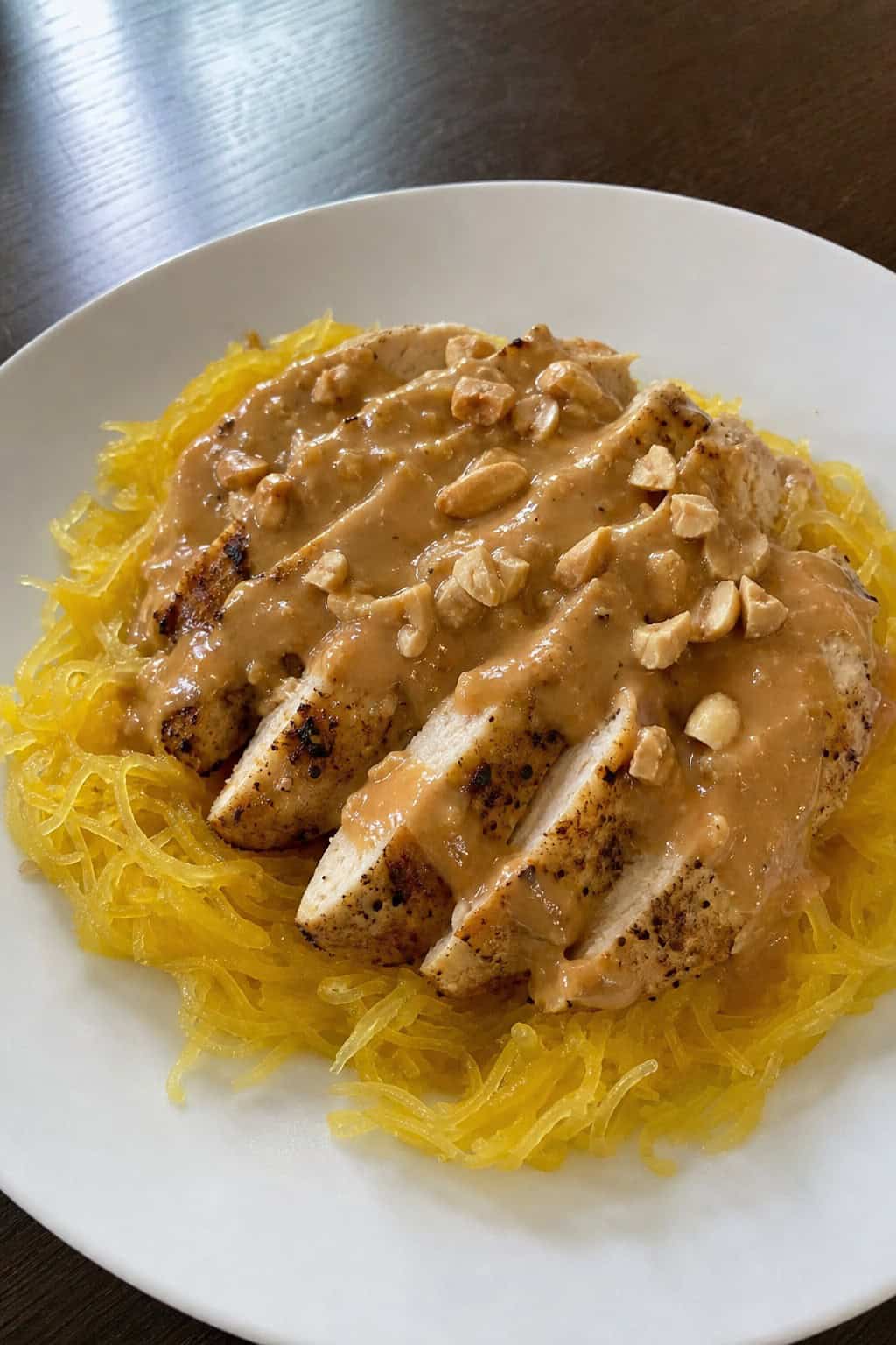 A plate of Thai peanut chicken served over roasted spaghetti squash garnished with peanuts and cilantro on a wooden table.