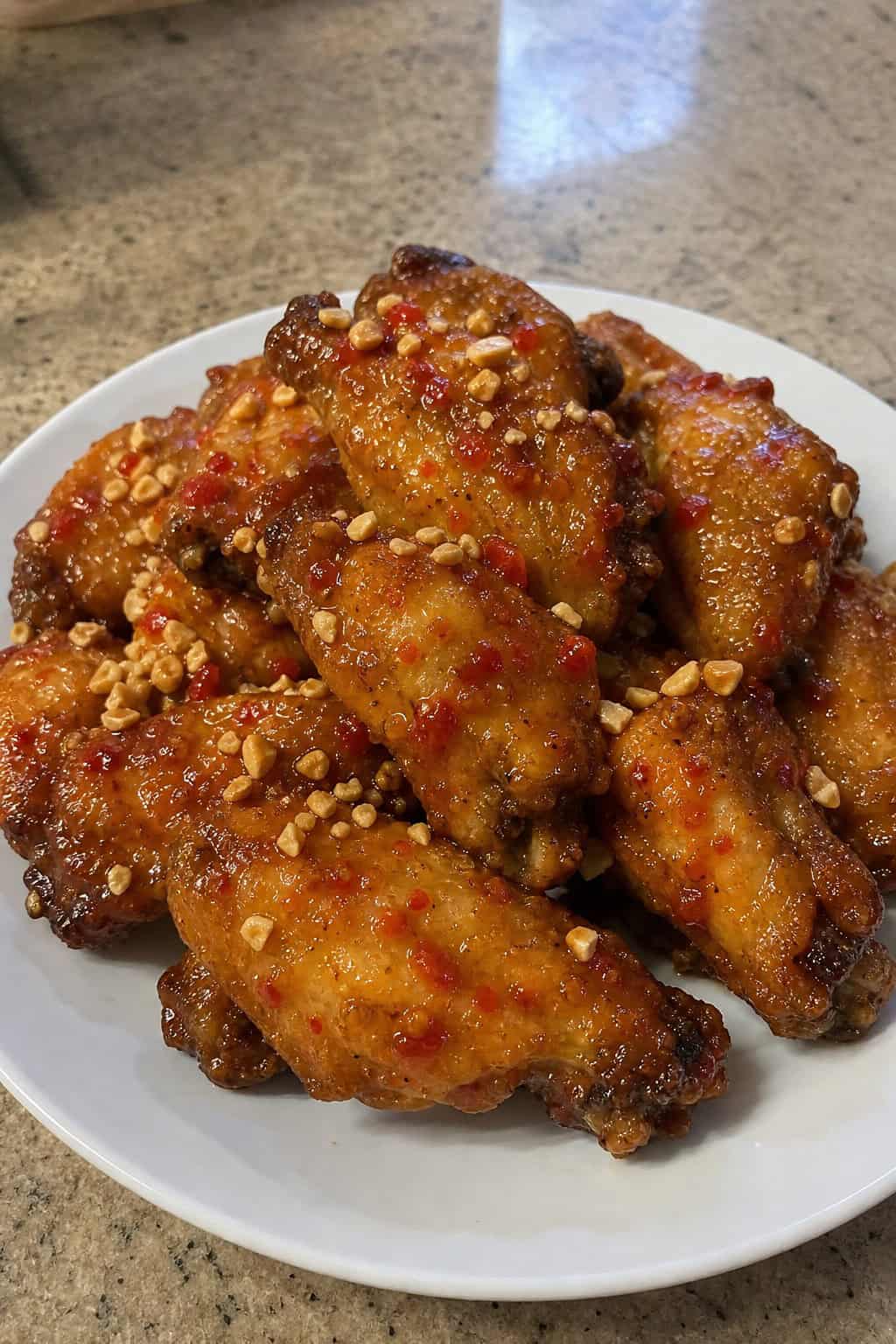 A platter of Thai sweet chili lime chicken wings garnished with crushed peanuts and lime wedges.