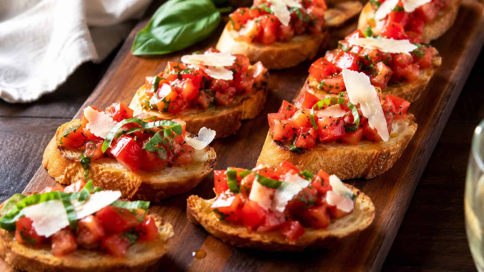 finished tomato basil bruschetta arranged on a wooden serving board, toasted baguette slices topped with diced red tomatoes and fresh sliced basil, shaved Parmesan, warm natural light, casual home entertaining