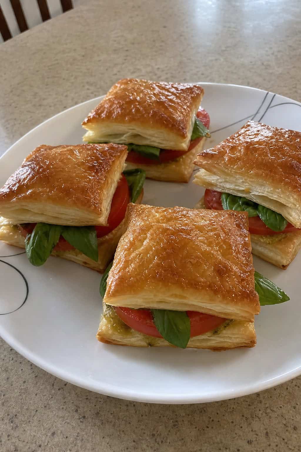 Plate of golden puff pastry squares layered with tomato slices and basil leaves on a wooden table.