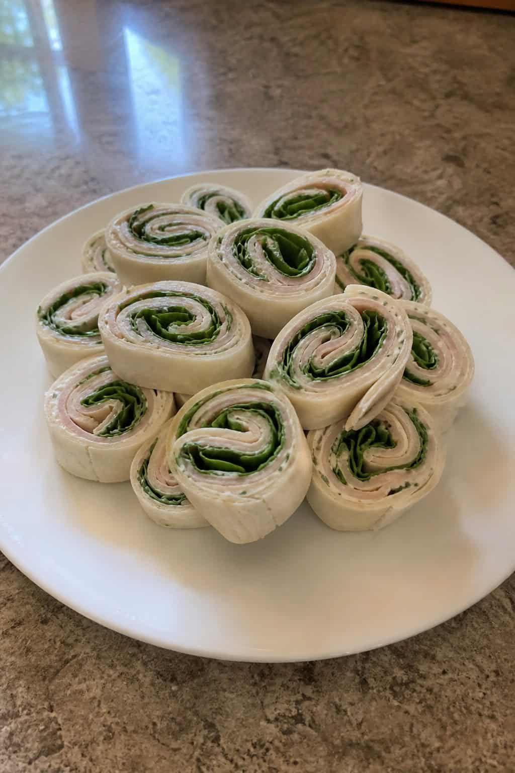 A plate of turkey ranch pinwheel appetizers showing visible layers of green spinach, shredded cheddar, and deli turkey inside sliced flour tortilla rolls.