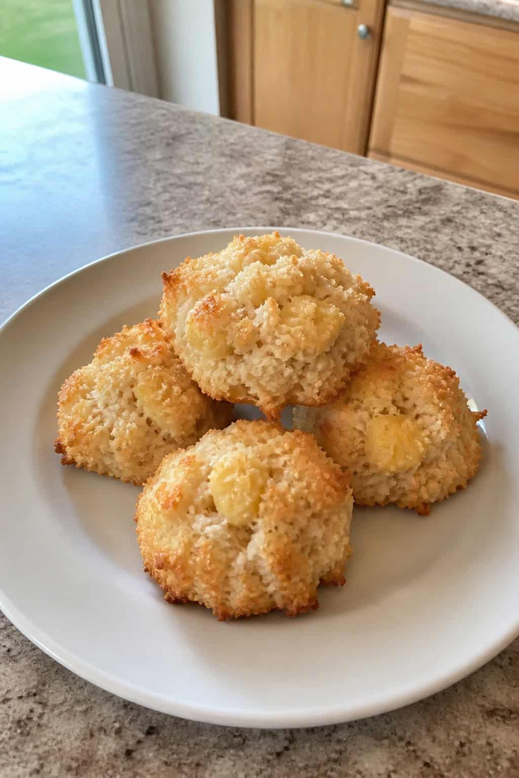 A plate of golden vegan banana coconut macaroons surrounded by fresh bananas and coconut halves on a wooden table.