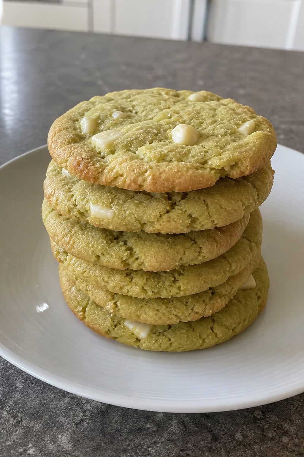 A stack of wasabi white chocolate shortbread cookies on a wooden plate with wasabi paste and white chocolate pieces nearby.