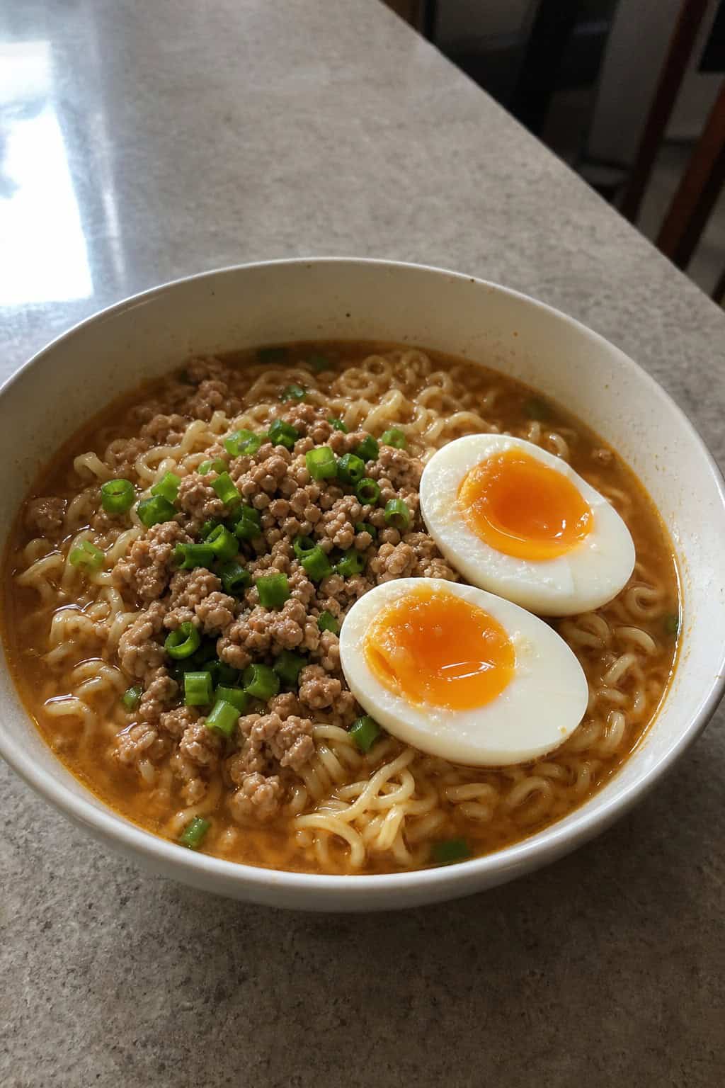 A bowl of minced chicken ramen with a soft-boiled egg, garnished with scallions and sesame seeds on a wooden table.