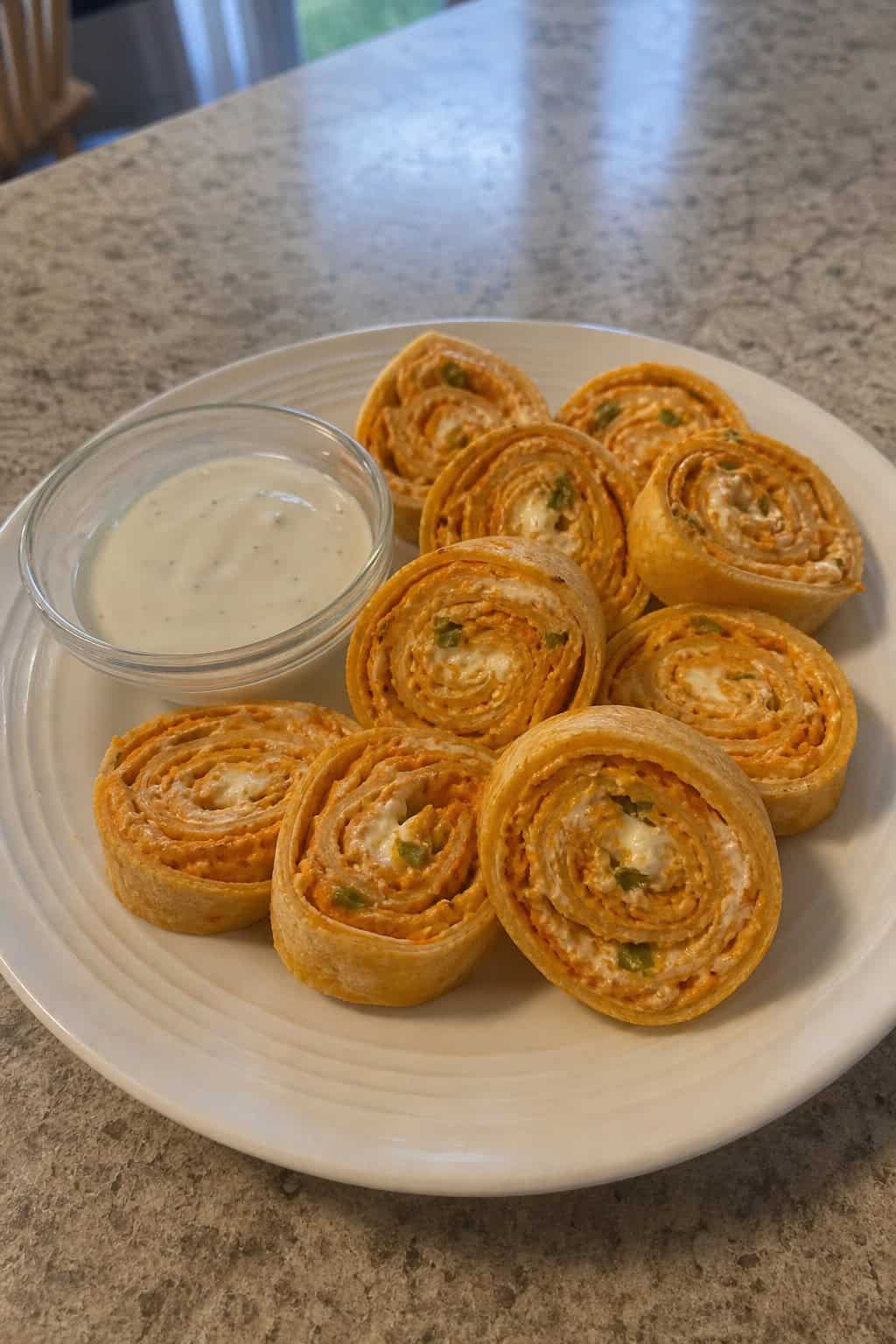 Buffalo Ranch Chicken Pinwheels arranged on a wooden board with celery sticks, carrot sticks, and a bowl of ranch dipping sauce.