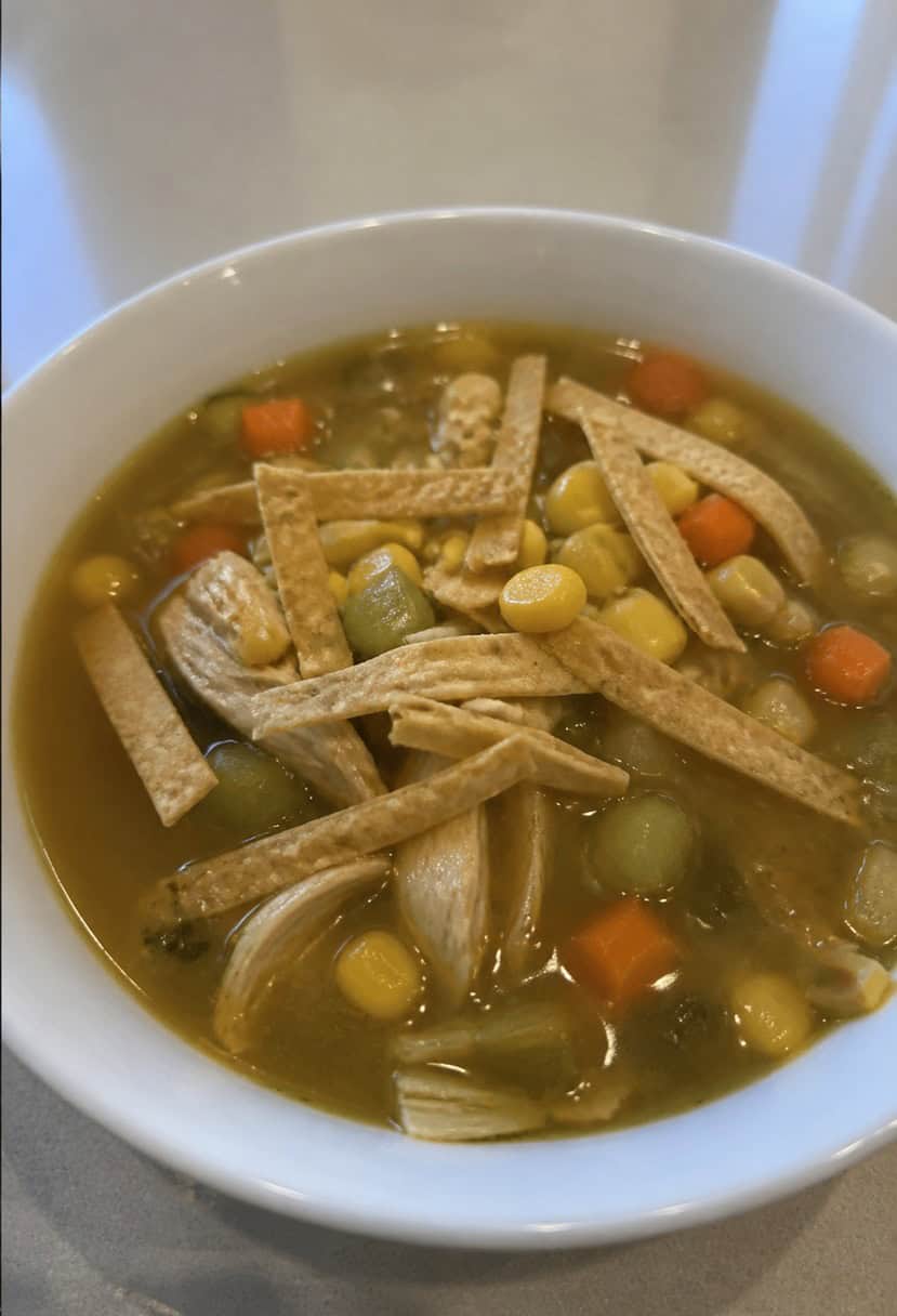 A steaming bowl of chicken tortilla soup surrounded by colorful vegetables and garnished with crispy tortilla strips