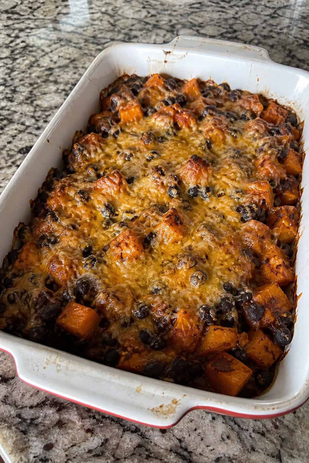 Sweet Potato Casseroles That Feed a Crowd 8 A baked sweet potato and black bean casserole garnished with cilantro and lime wedges on a wooden table with small bowls of ingredients nearby.