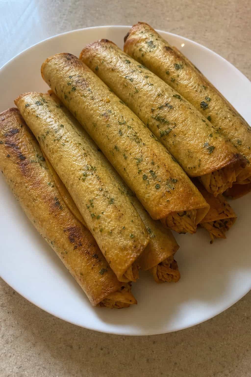A plate of crispy cilantro-lime chicken taquitos with lime wedges and a bowl of dipping sauce on a wooden table.
